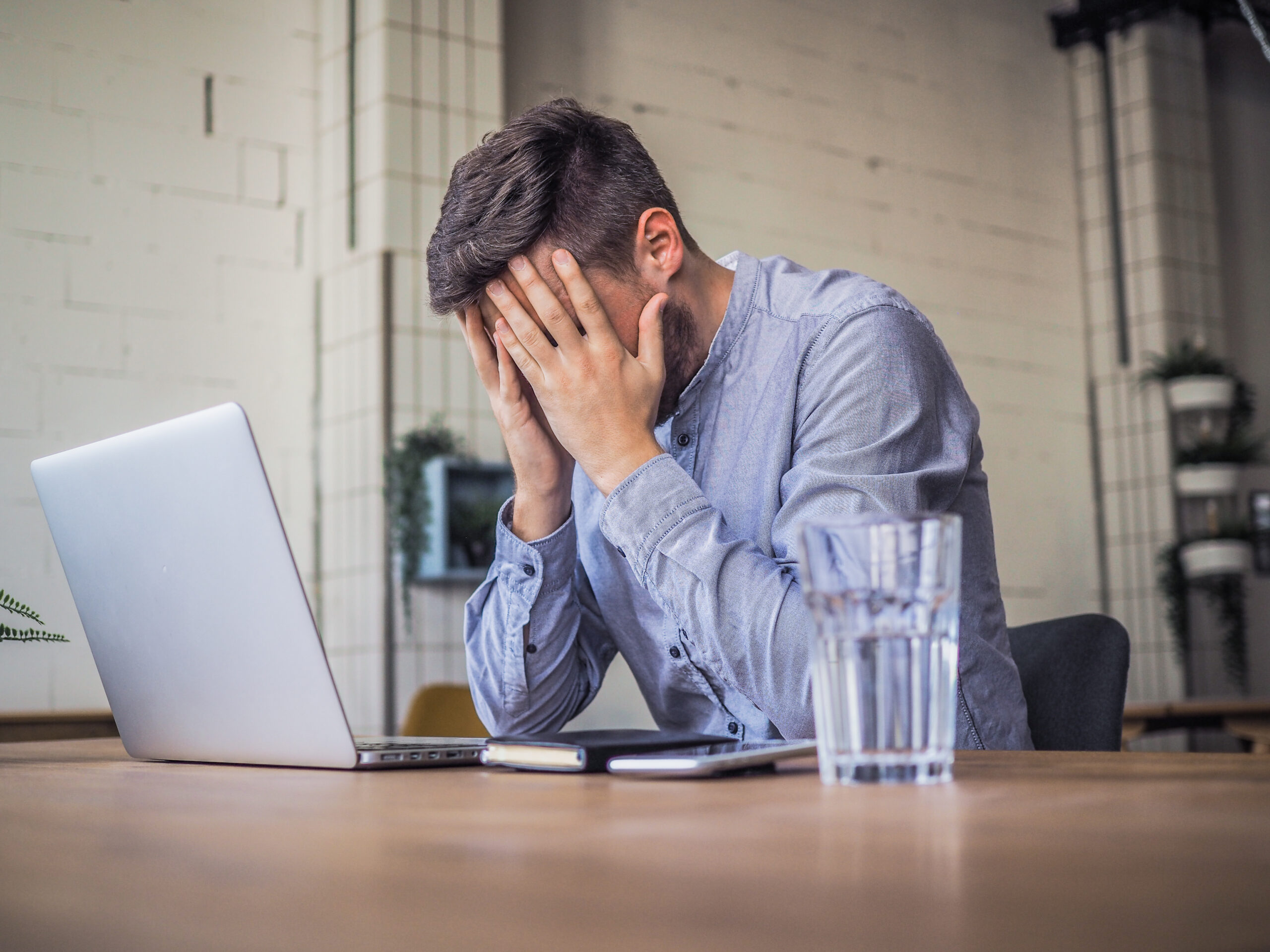 worried and disappointed remote online working man in casual outfit with laptop sitting in an coworking / home office at a work desk